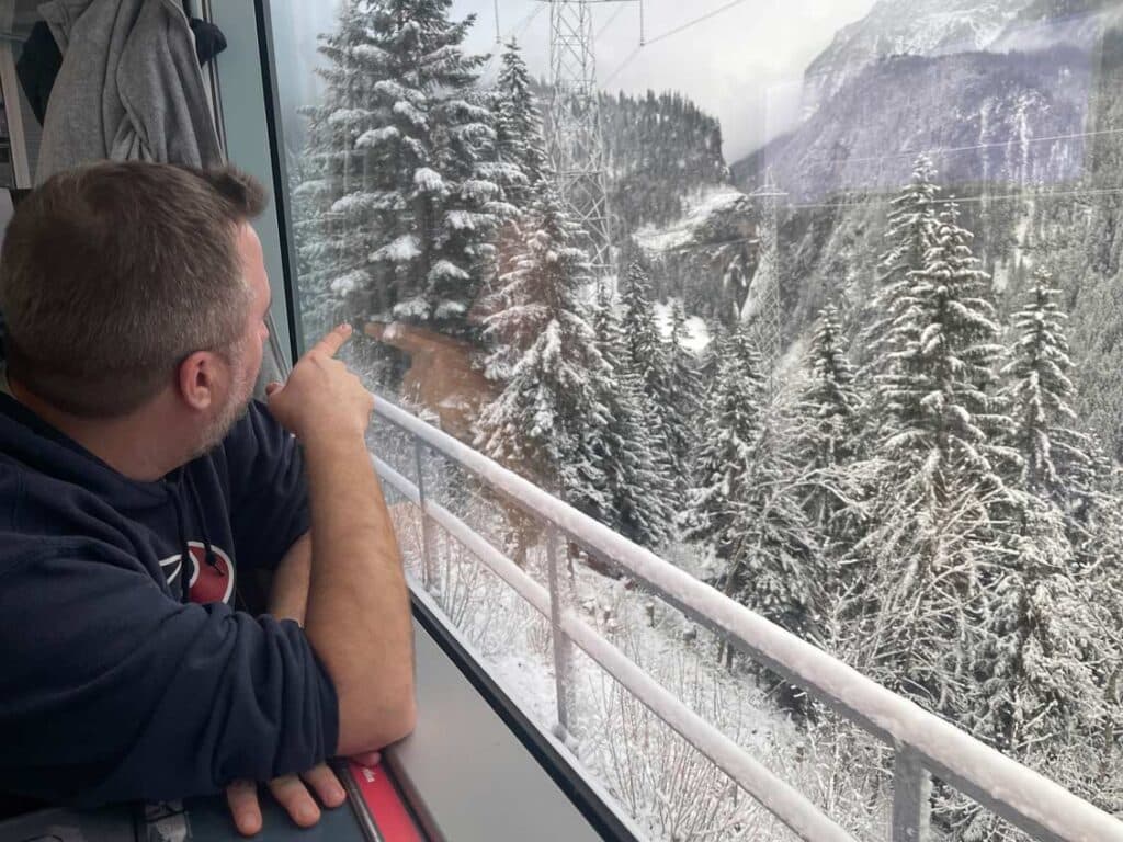 Bernina Express vs. Regionalbahn: Tipps für die perfekte Zugreise durch die Schweizer Alpen mann-blickt-aus-fenster-in-der-regionalbahn-auf-bernina-express-route-auf-schneetannen