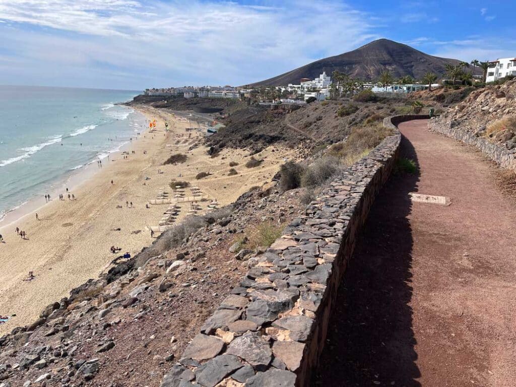 Unsere Top 11 Strände auf Fuerteventura fussgaengerweg-laeuft-auf-vulkanberg-zu-links-davon-sandstrand-und-meer