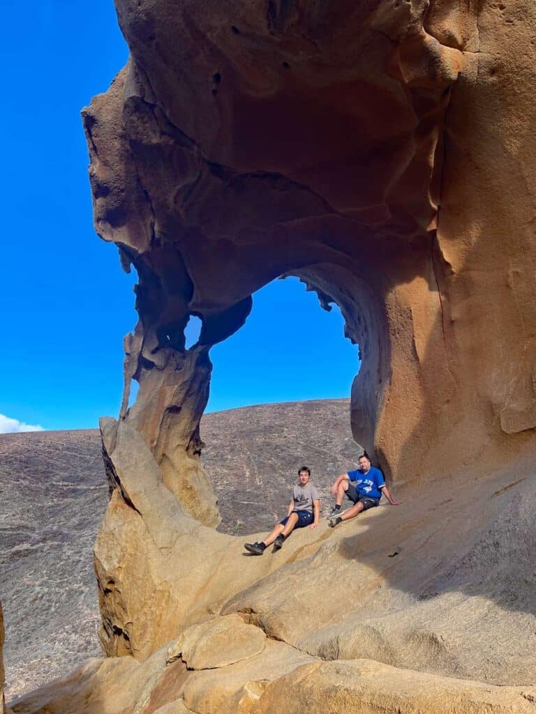 14+ Fuerteventura Sehenswürdigkeiten für den Familienurlaub vater und sohn sitzen im arco de las penitas auf fuerteventura