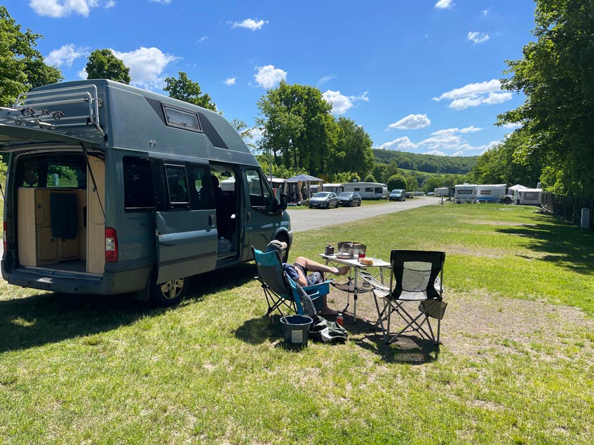 Biggesee Camping: 7+ Tipps für den See im Sauerland mann auf campingstuhl neben einem Van auf dem vier jahreszeiten campingplatz am biggesee im sauerland