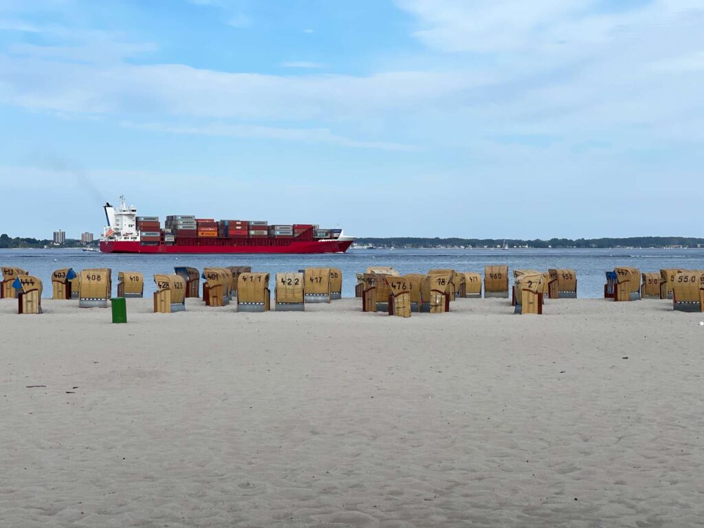 containerschiff fährt an weißem sandstrand mit strandkörben in laboe