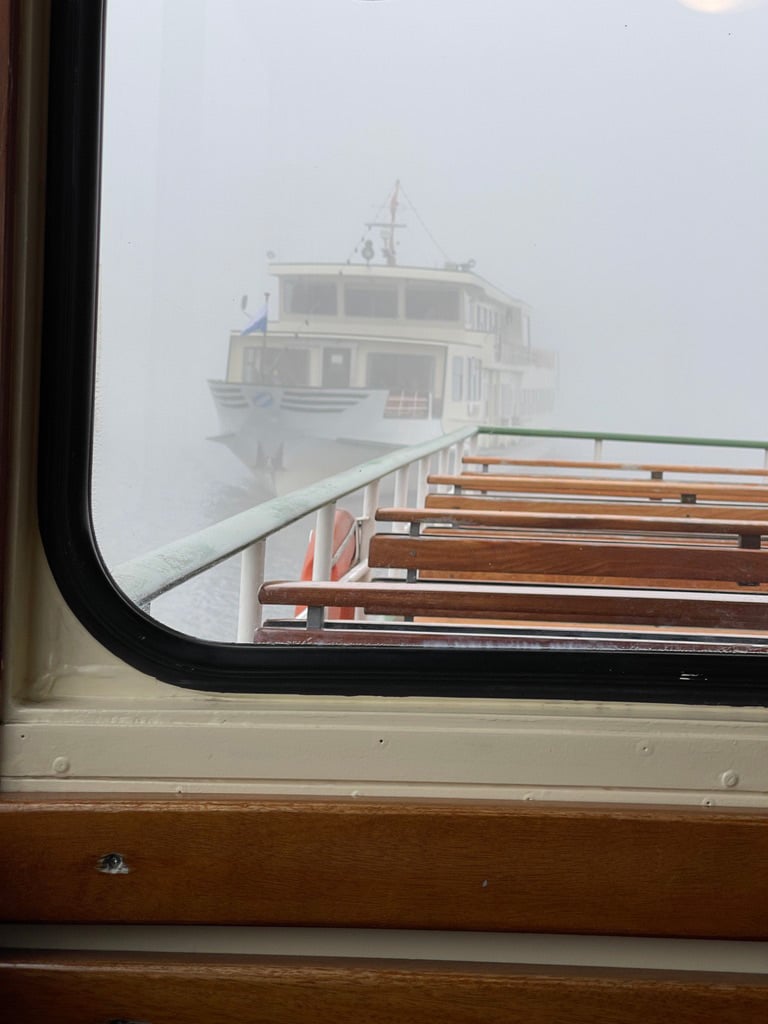 blick über leere sitzbänke im schiff über den nebel auf dem chiemsee kommt ein anderes schiff