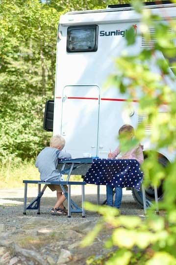 zwei kinder sitzen an einem tisch vor einem wohnmobil und lernen auf reisen