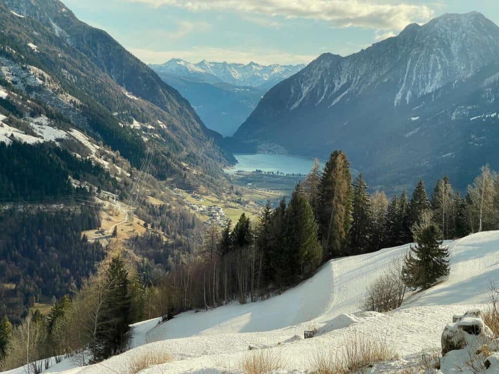 verschneite landschaft aus dem zugfenster, unten blauer see während der fahrt mit dem bernina express