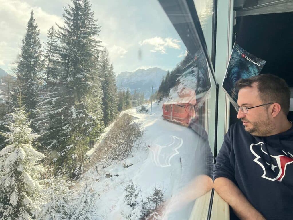 Mann schaut aus dem Zugfenster in verschneite Landschaft während der Fahrt mit dem Berninaexpress