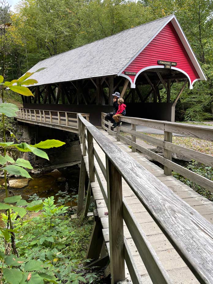 zwei kinder vor überdachter roter brücke in neuengland