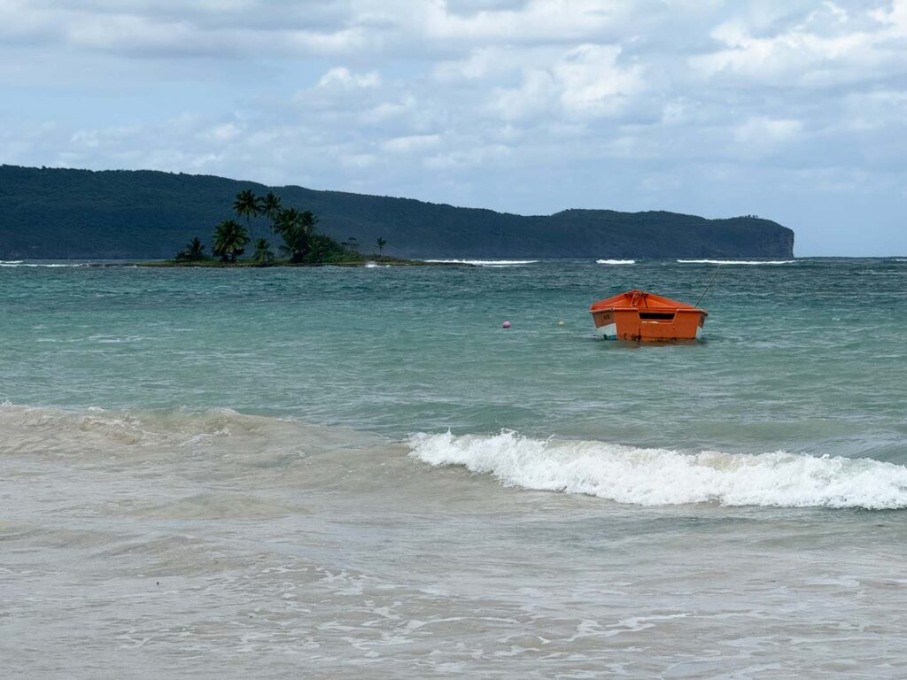 rotes boot im meer dahinter insel mit palmen vor bergkette