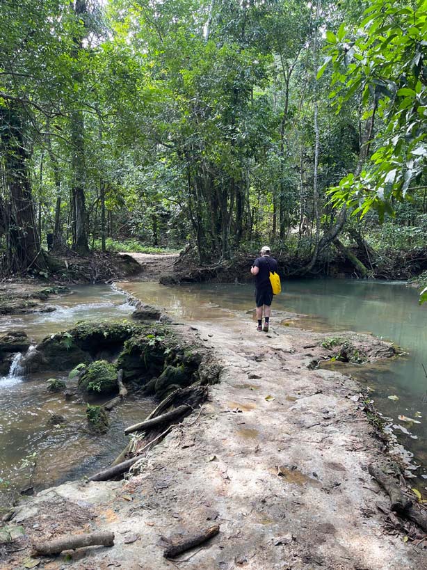 mann läuft auf überflutetem weg über einen fluss auf dem weg zum wasserfall salto el limon
